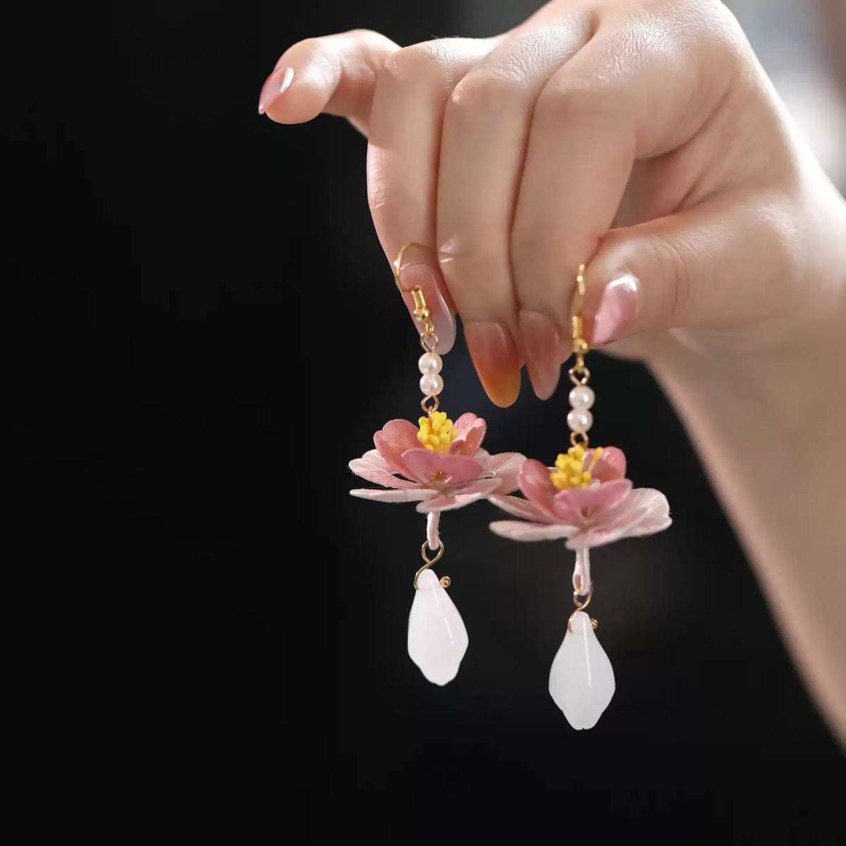 Pair of lotus drop earrings held in hand