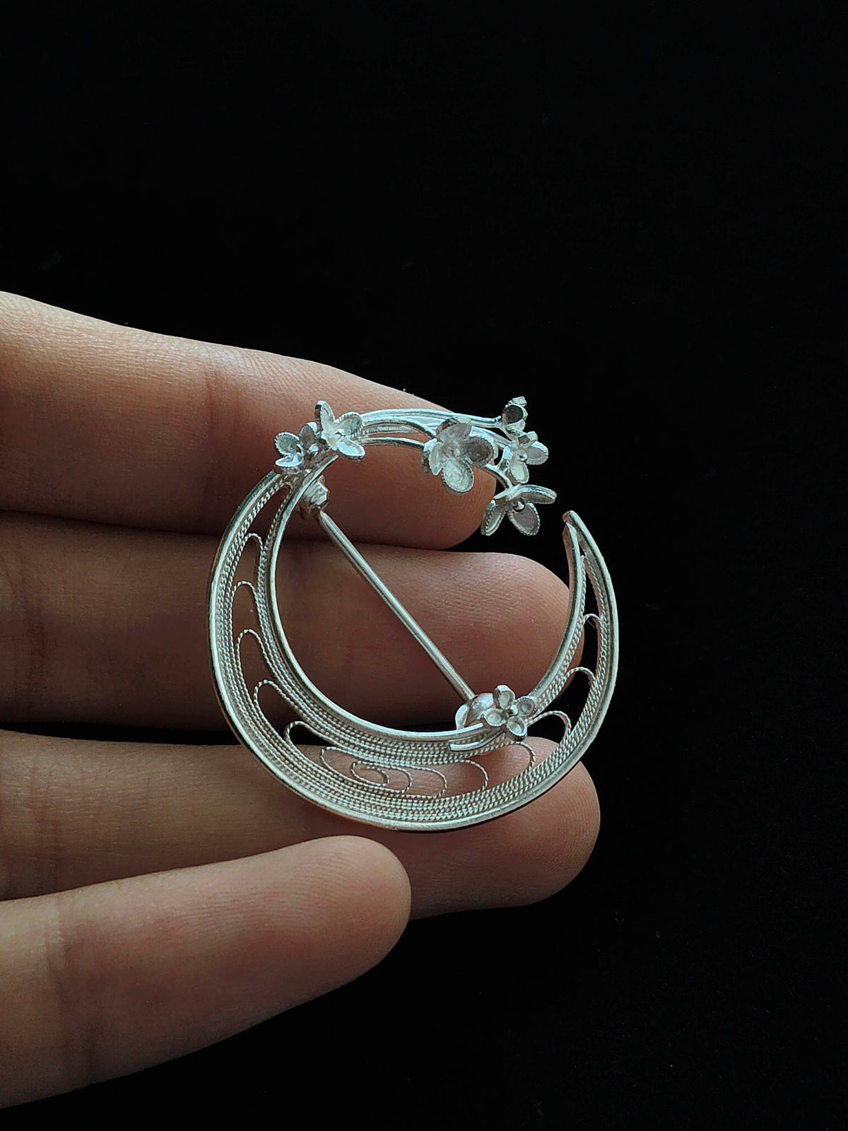 Front view of a silver-tone crescent moon brooch with openwork floral branches, held to show its details