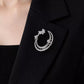 Silver-tone openwork crescent moon brooch with small flower details pinned to a dark lapel