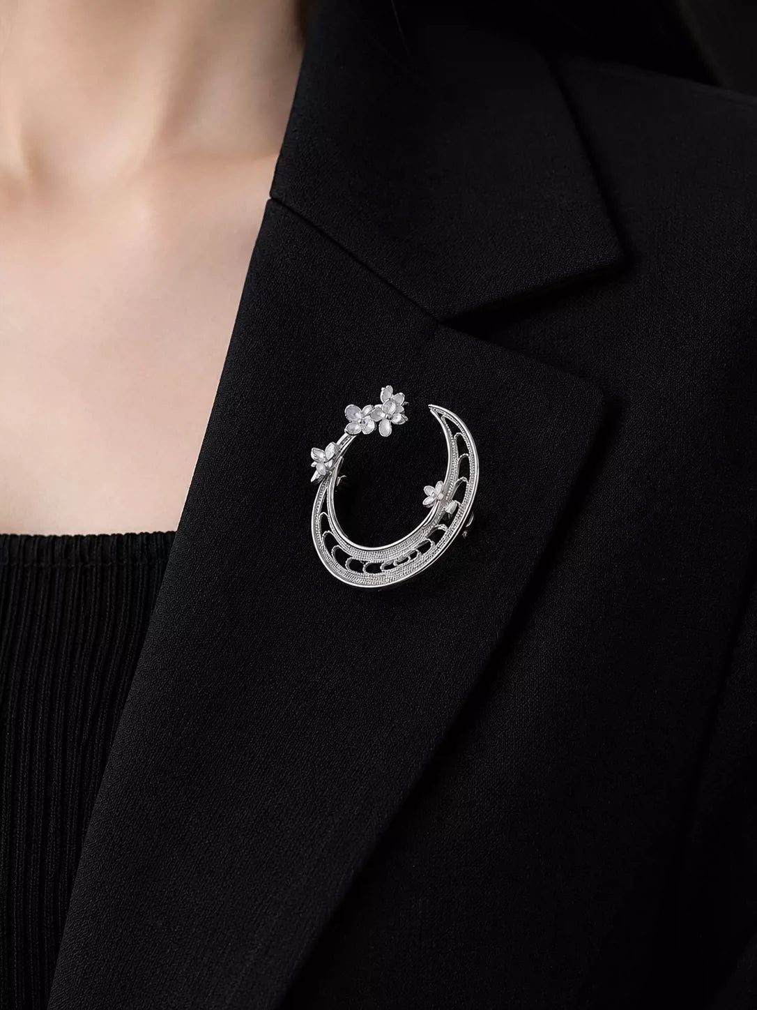 Silver-tone openwork crescent moon brooch with small flower details pinned to a dark lapel