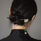 Dark wood hair stick securing a bun, with green and gold accents