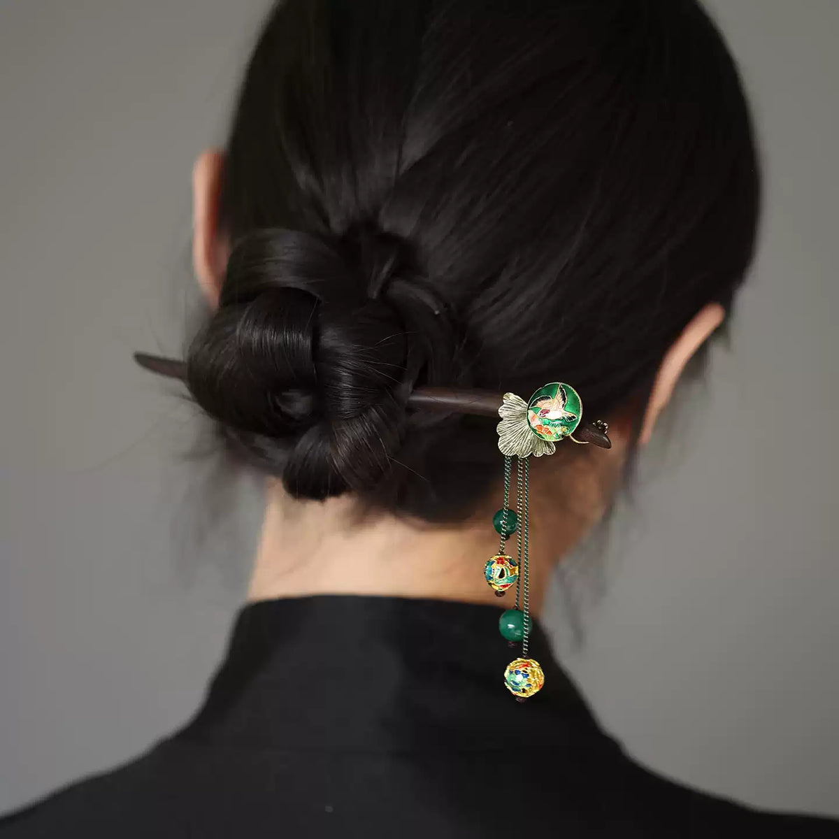 Dark wood hair stick securing a bun, with green and gold accents