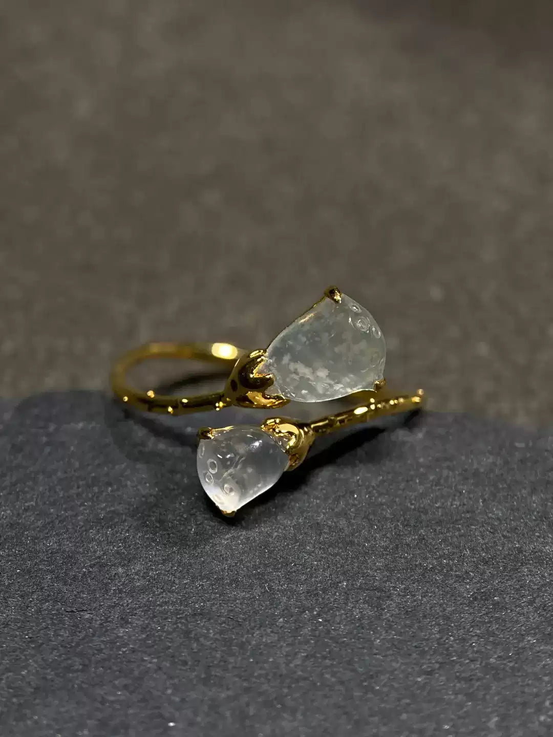 Gold-tone open ring with two translucent lotus pod accents on a dark display surface