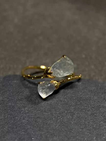 Gold-tone open ring with two translucent lotus pod accents on a dark display surface