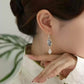 Butterfly drop earring with a white teardrop pendant shown worn with a light-colored outfit