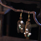 Pair of irregular drop earrings with decorative accents, shown on a display branch.
