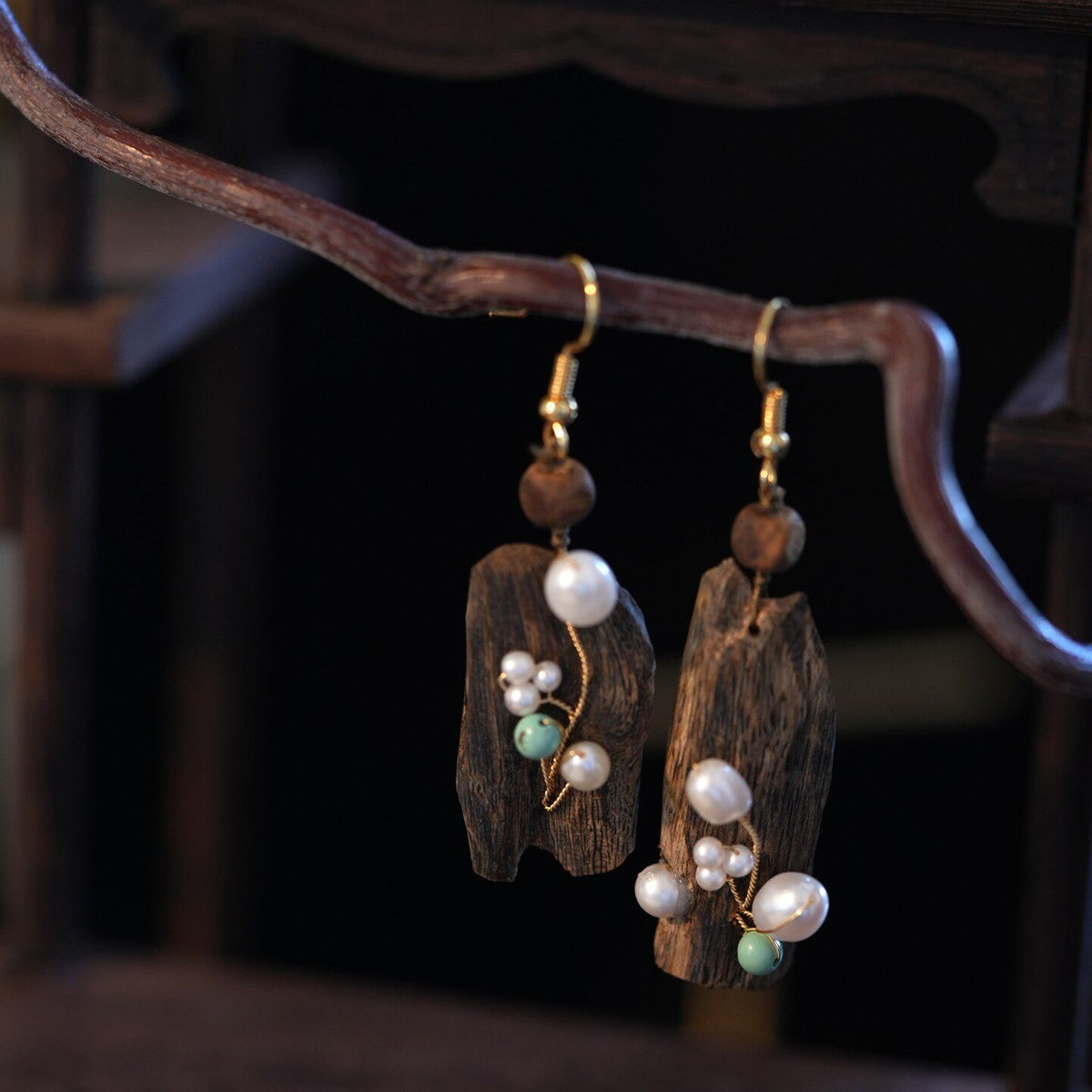 Pair of irregular drop earrings with decorative accents, shown on a display branch.