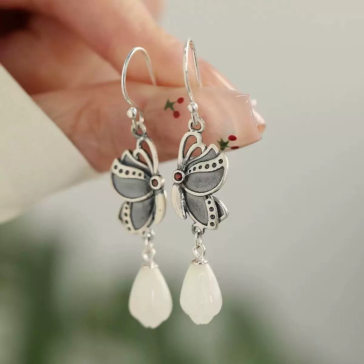 Pair of butterfly-shaped drop earrings with silver-tone outlines and white teardrop pendants
