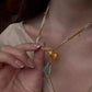 Close-up of a gold-tone double-layer gourd necklace with pale bead accents and a blue-green tassel