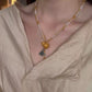 Gold-tone necklace with gourd pendant and blue-green tassel, worn with a light outfit