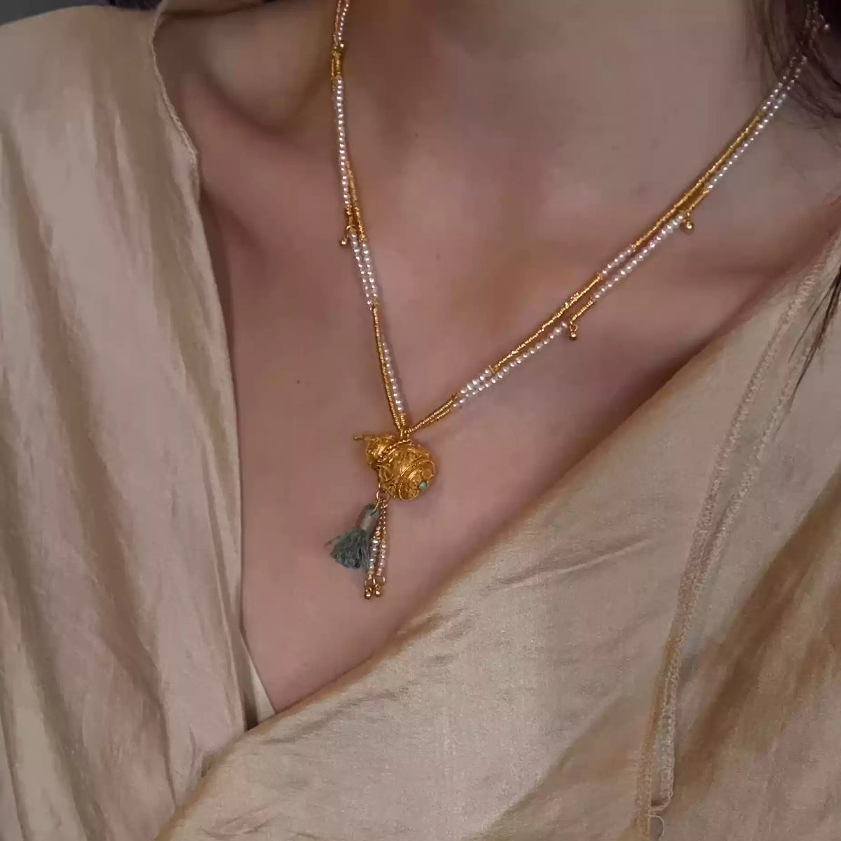 Layered gold-tone necklace with pale bead accents and detailed gourd pendant