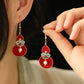 Red gourd earrings with turquoise floral details, worn and held in hand