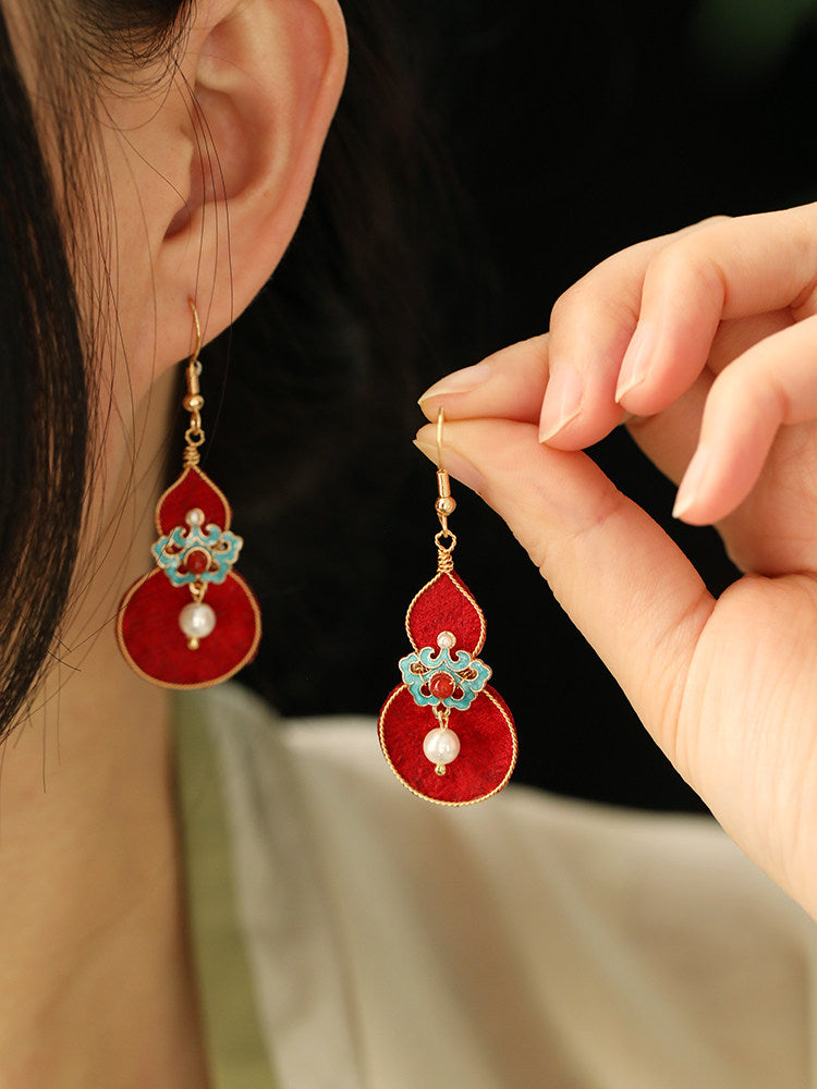 Red gourd earrings with turquoise floral details, worn and held in hand