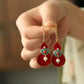 Pair of red gourd drop earrings displayed in hand