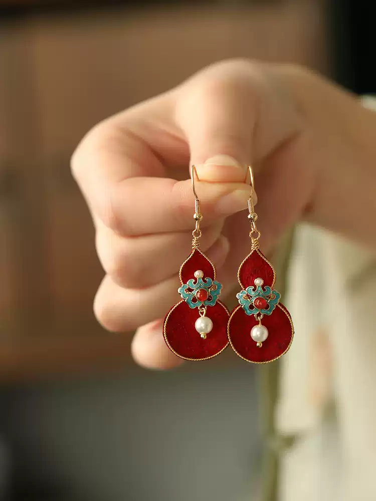 Pair of red gourd drop earrings displayed in hand
