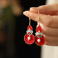 Close-up of the red gourd earrings with gold-tone hooks and white bead accents