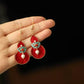 Red gourd and turquoise floral earrings shown against a hand