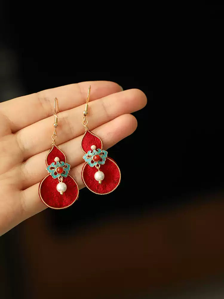Red gourd and turquoise floral earrings shown against a hand