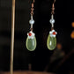 Long green agate and freshwater pearl earrings hanging on a display stand