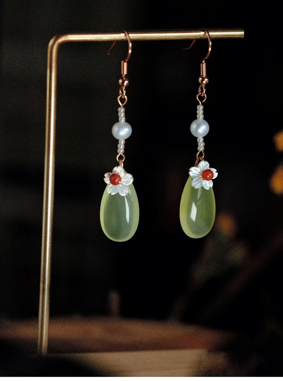 Long green agate and freshwater pearl earrings hanging on a display stand
