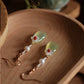 Mother-of-pearl flower and green agate earrings displayed on a wooden tray