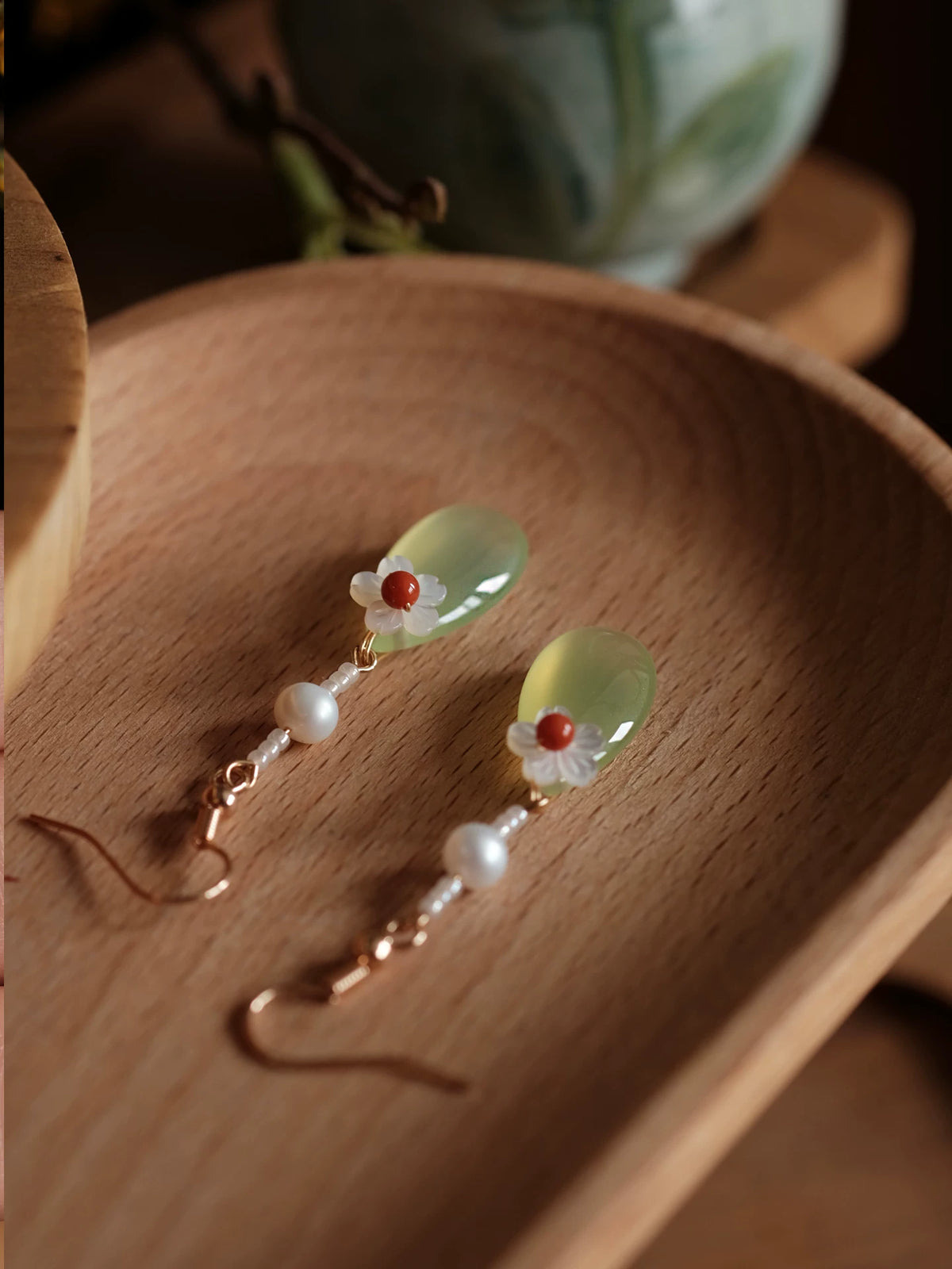 Mother-of-pearl flower and green agate earrings displayed on a wooden tray