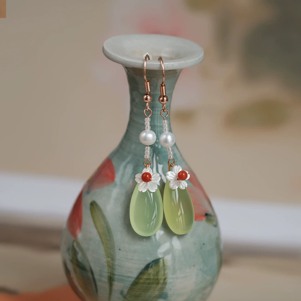 Green agate and pearl earrings displayed on a floral ceramic vase