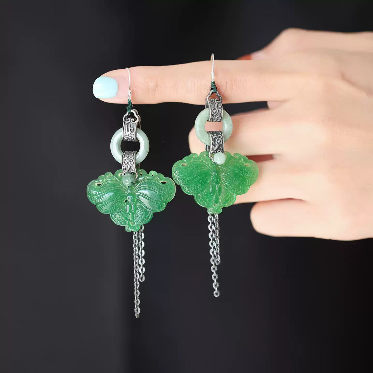 Pair of green butterfly jade-style tassel earrings held in hand