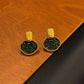 Pair of green and gold-tone garden-window stud earrings on a wood surface