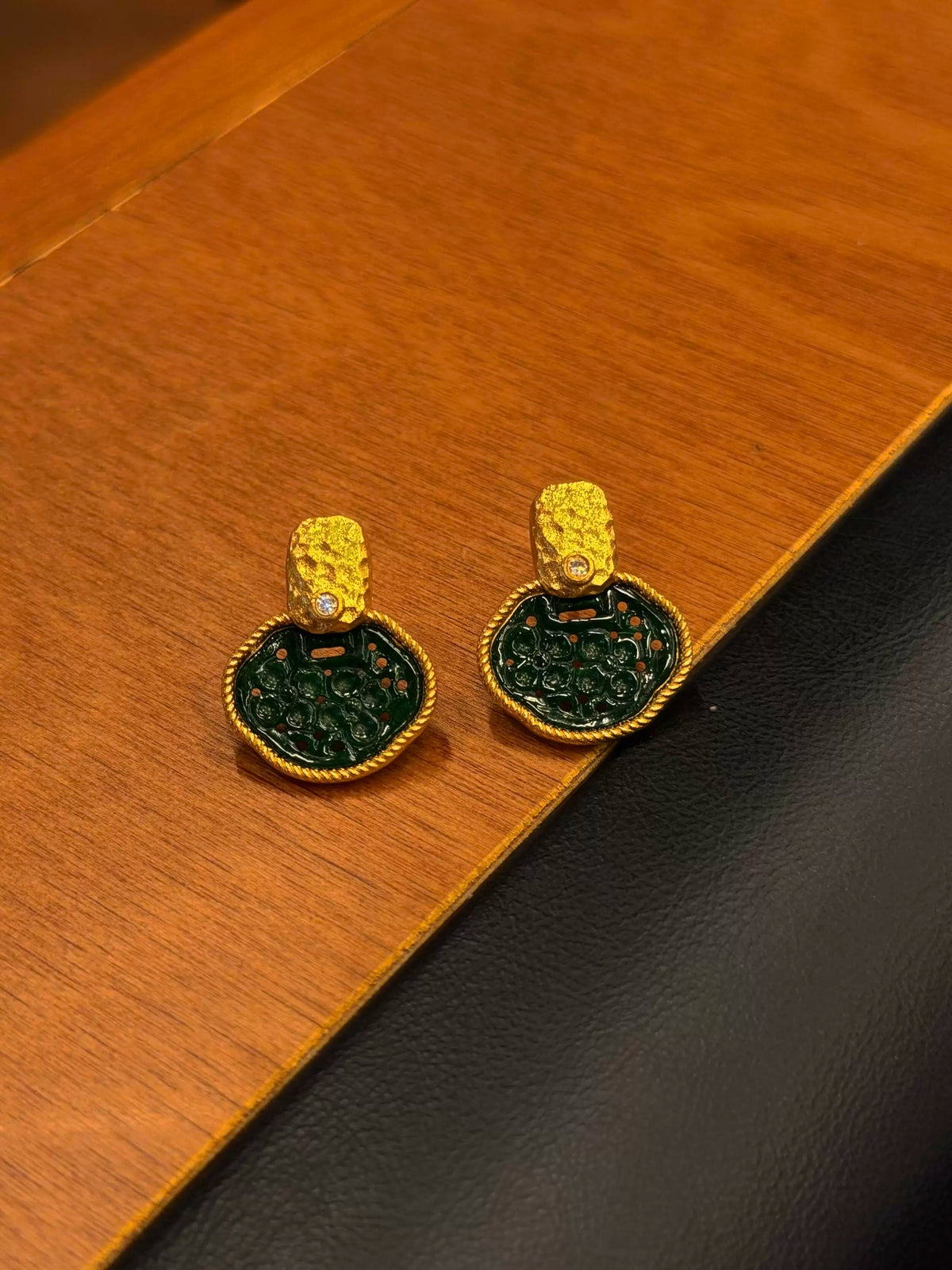 Pair of green and gold-tone garden-window stud earrings on a wood surface