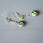 Pair of green floral earrings arranged diagonally on a neutral background