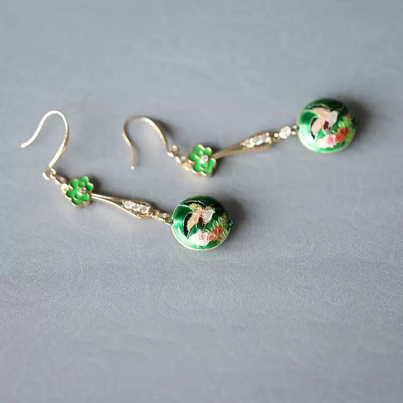 Pair of green floral earrings arranged diagonally on a neutral background