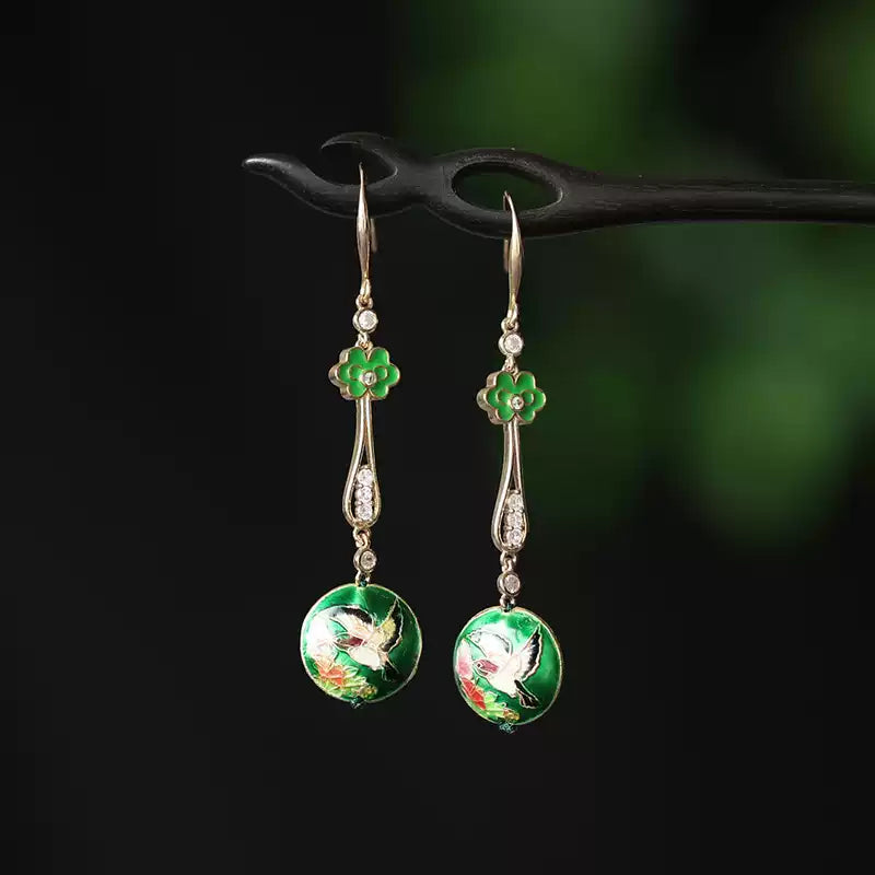 Pair of long green floral earrings displayed against a dark green background