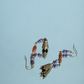 Hua Ling bell earrings with purple beads and patterned charms reflected on a mirror, angle view
