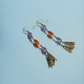 Hua Ling bell earrings with purple beads and patterned charms reflected on a mirror, detail view
