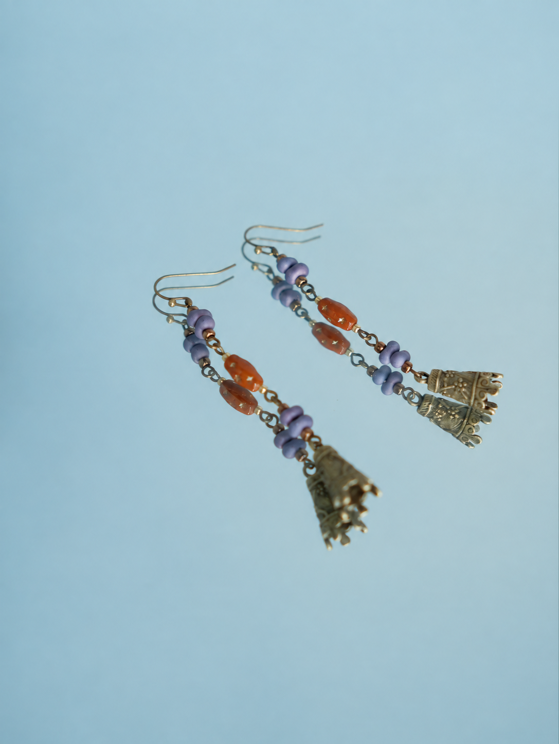 Hua Ling bell earrings with purple beads and patterned charms reflected on a mirror, detail view