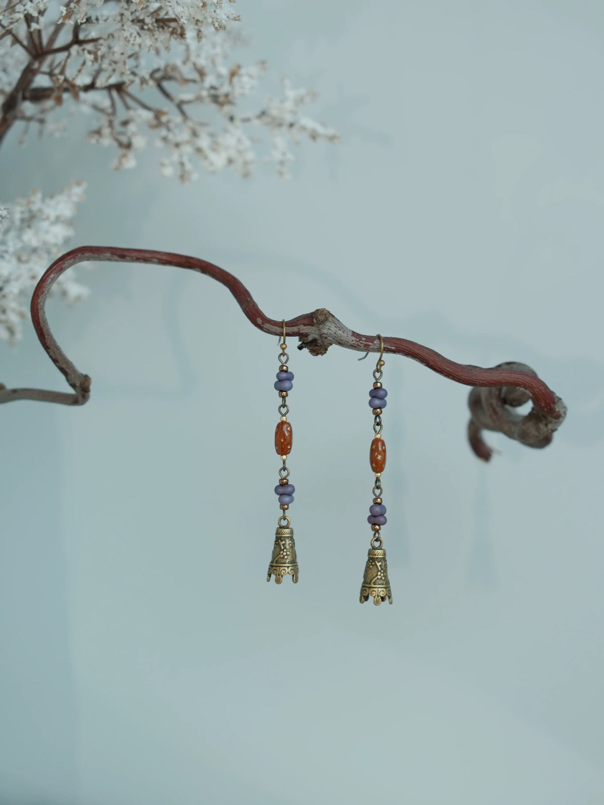 Full-length pair of Hua Ling bell drop earrings on a pale blue background