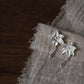 Pair of lily flower copper earrings with drop details on a neutral fabric display