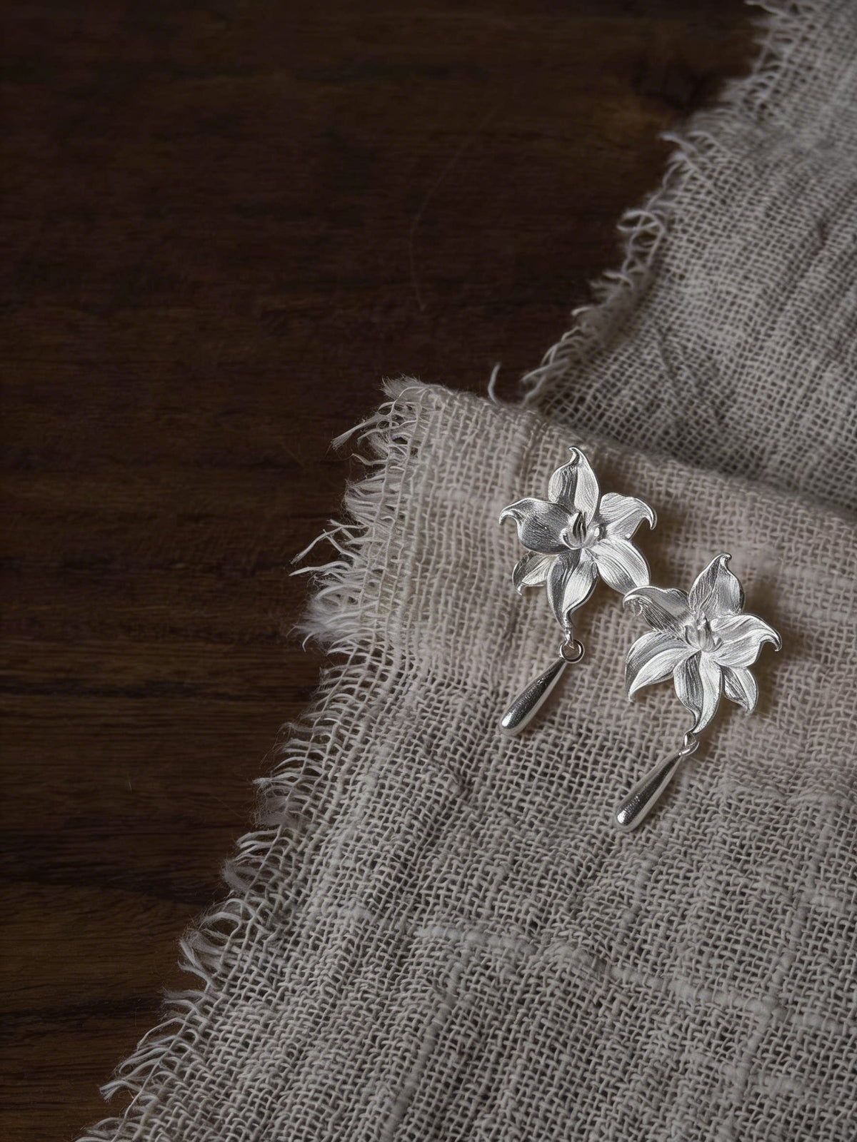 Pair of lily flower copper earrings with drop details on a neutral fabric display