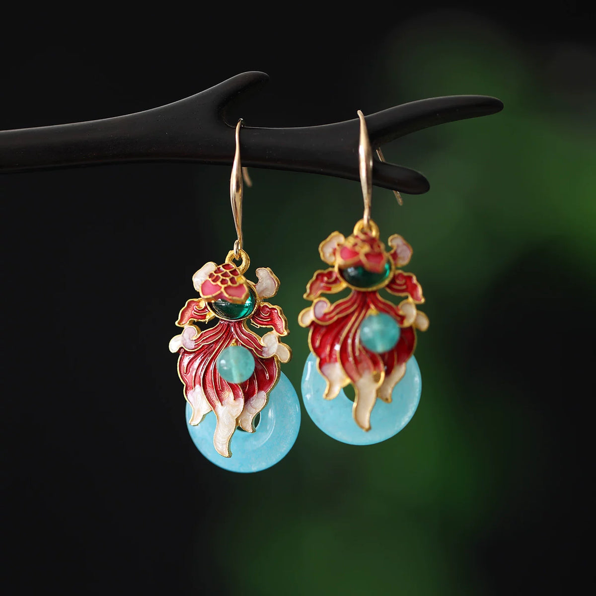 Pair of colorful koi fish drop earrings on a dark display branch