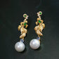 Gold-tone koi fish earrings with decorative stones and pearl-look drops against a dark background