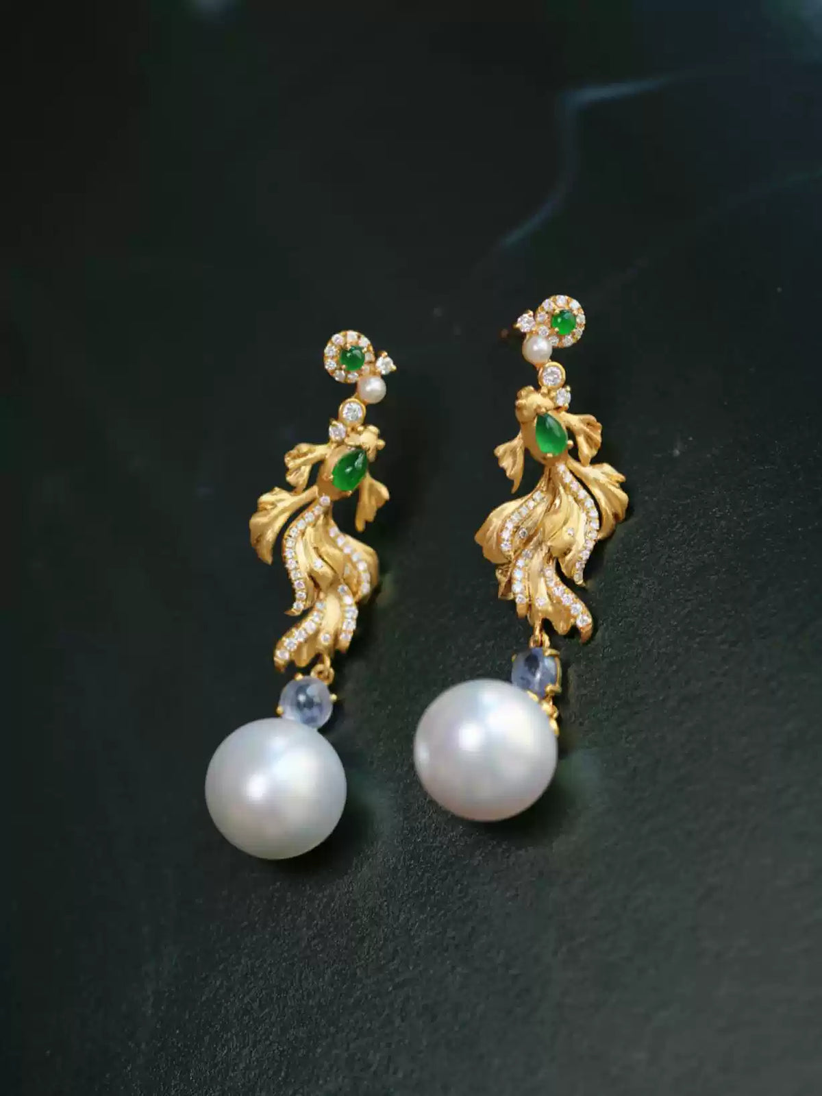 Gold-tone koi fish earrings with decorative stones and pearl-look drops against a dark background
