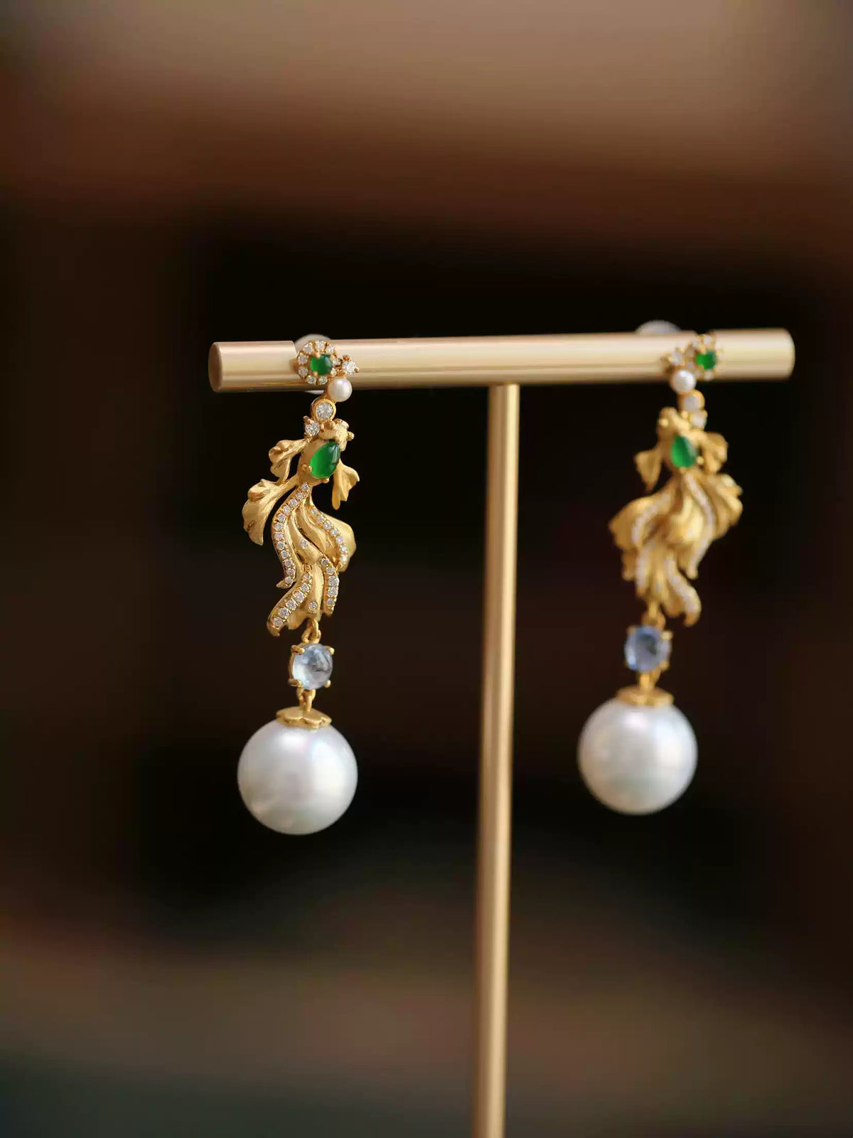 Close view of gold-tone koi earrings showing green imitation jade accents and filigree detail