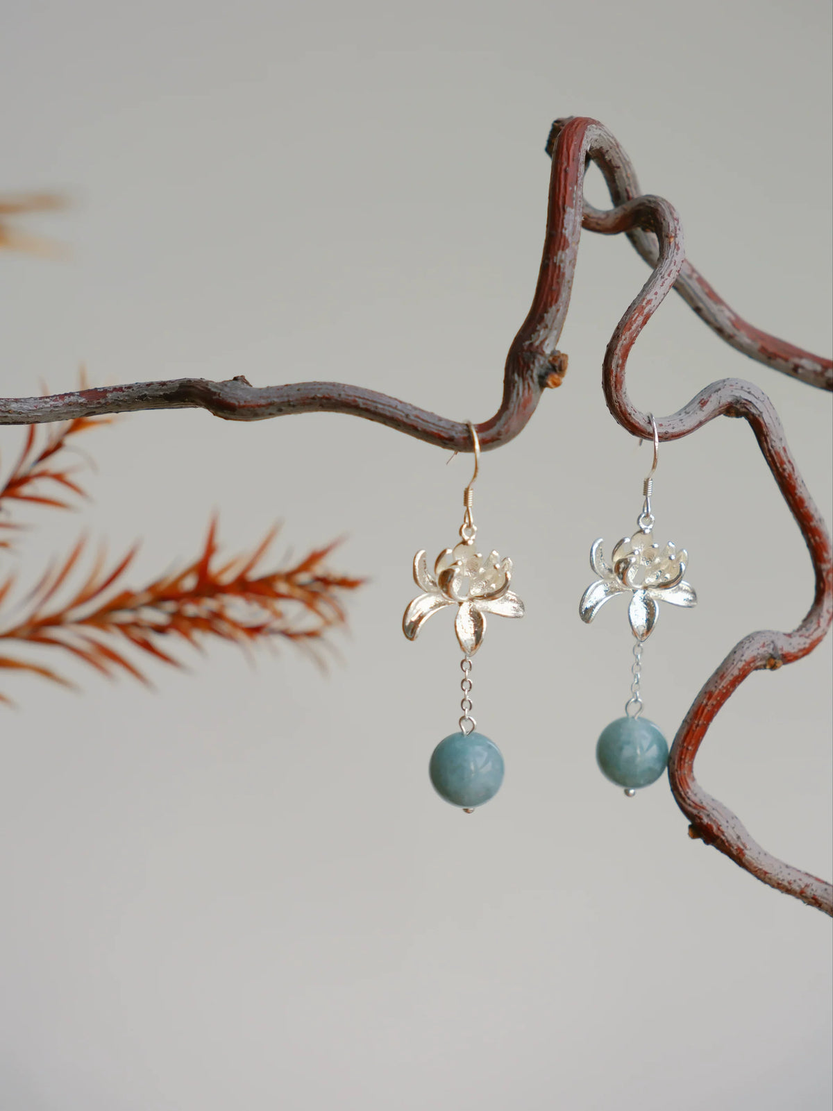Pair of lotus flower drop earrings hanging from a branch, hook style