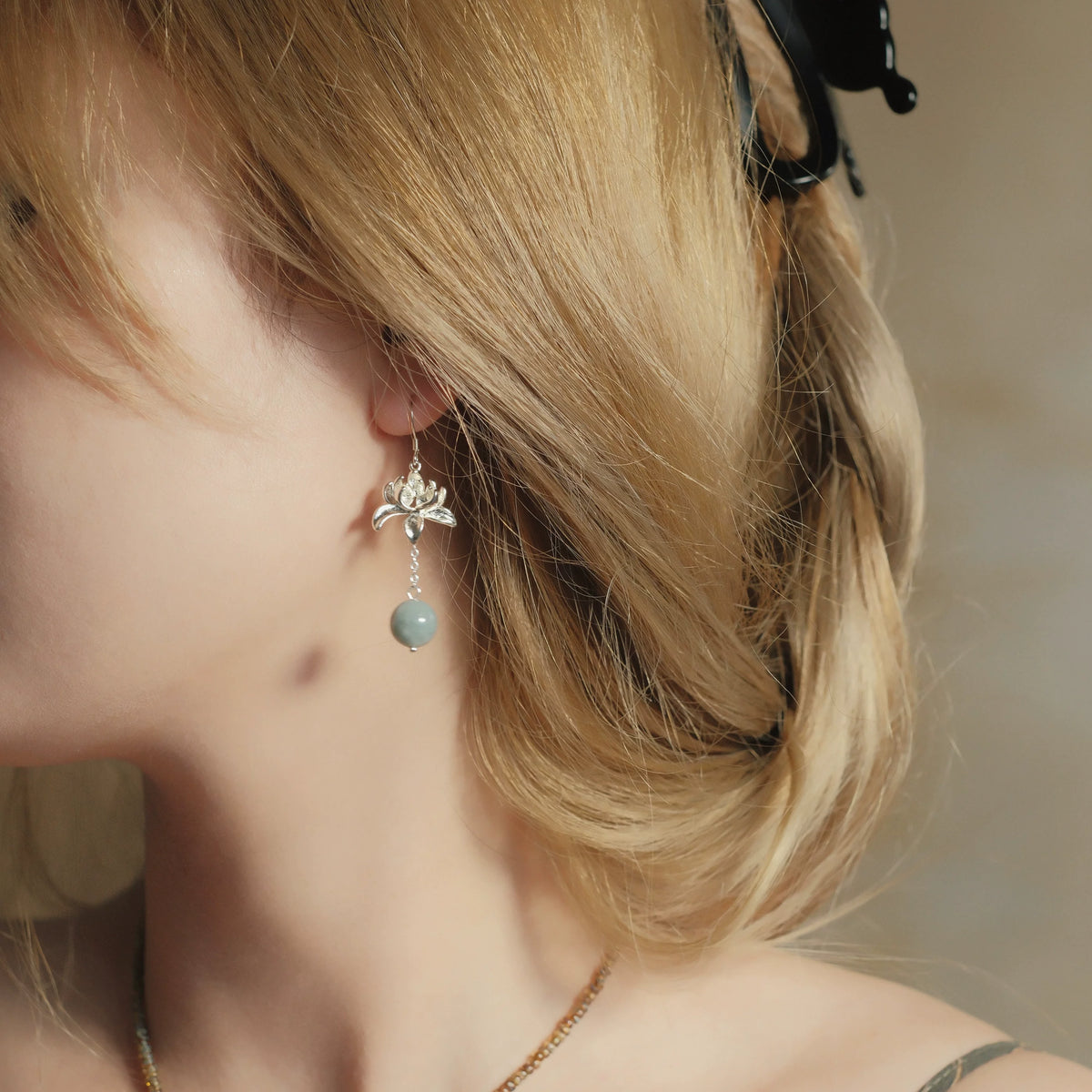 Close-up of Lian Yi lotus and blue-green bead earring worn with a silver hook