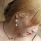 Side view of a silver-tone lotus drop earring with a blue-green bead