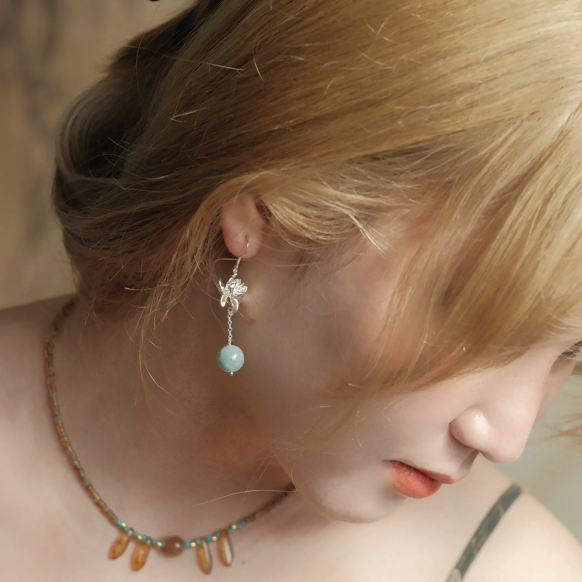 Side view of a silver-tone lotus drop earring with a blue-green bead