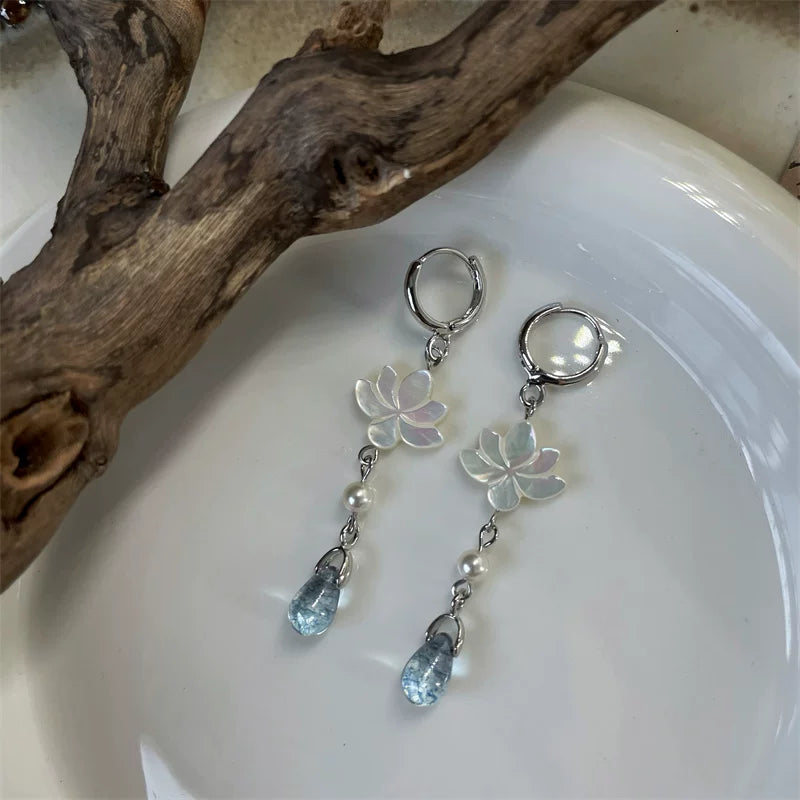 Mother-of-pearl lotus hoop earrings with blue-gray glass drops on a ceramic dish