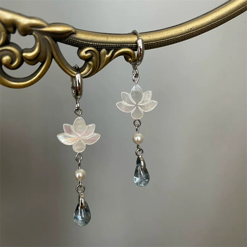 Lotus drop earrings hanging from a decorative brass display