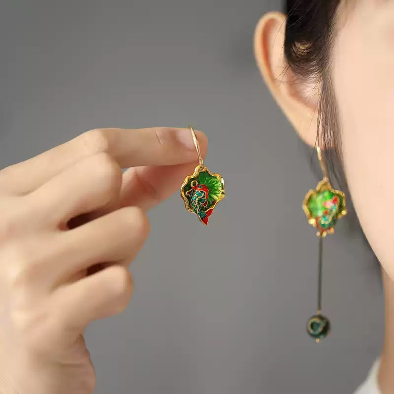 Green koi enamel-style drop earring shown beside a hand